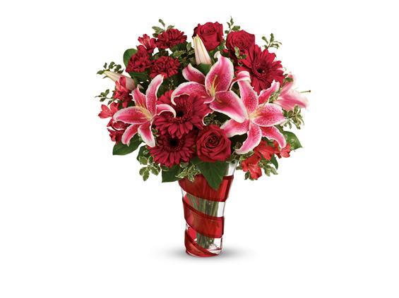 Flower arrangement in red swirl vase with Red roses, hot pink oriental lilies, red gerberas, and red carnations are arranged with pitta negra and lemon leaf flowers