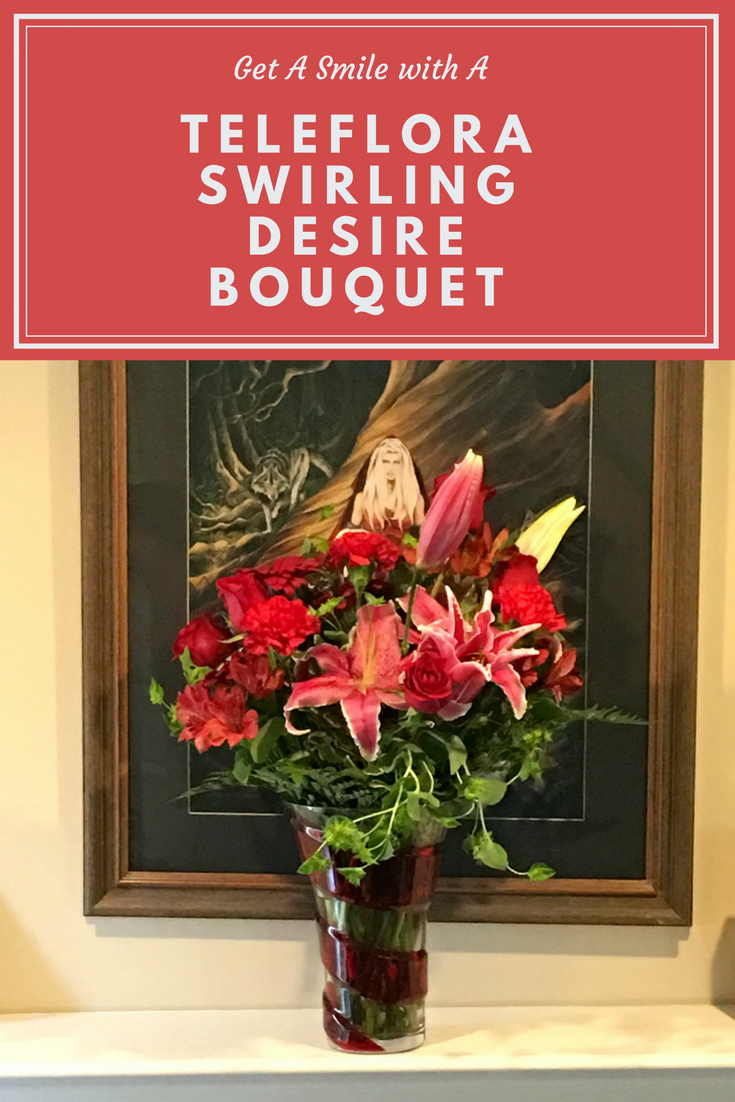 Flower arrangement in red swirl vase with Red roses, hot pink oriental lilies, red gerberas, and red carnations are arranged with pitta negra and lemon leaf flowers on a fireplace