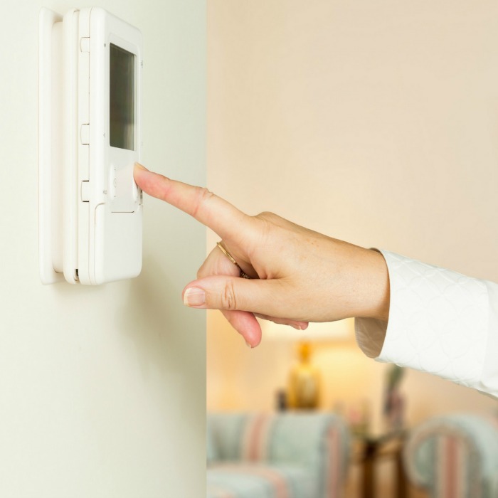 woman's hand turning down thermostat