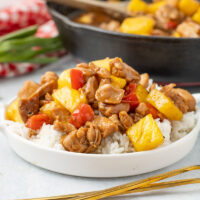 picture of freshly made pineapple chicken in a white bowl with a cast iron pan in the background