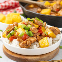 picture of freshly made pineapple chicken in a white bowl with a cast iron pan in the background