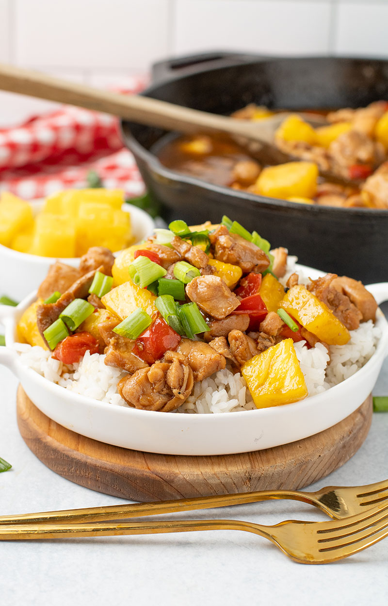 picture of freshly made pineapple chicken in a white bowl with a cast iron pan in the background
