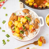 picture of freshly made pineapple chicken in a white bowl with a cast iron pan in the background