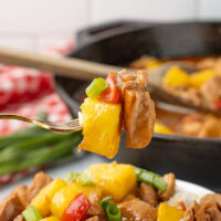 picture of freshly made pineapple chicken in a white bowl with a cast iron pan in the background