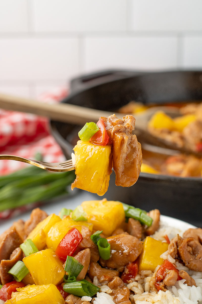 picture of freshly made pineapple chicken in a white bowl with a cast iron pan in the background