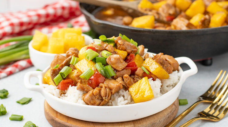 picture of freshly made pineapple chicken in a white bowl with a cast iron pan in the background