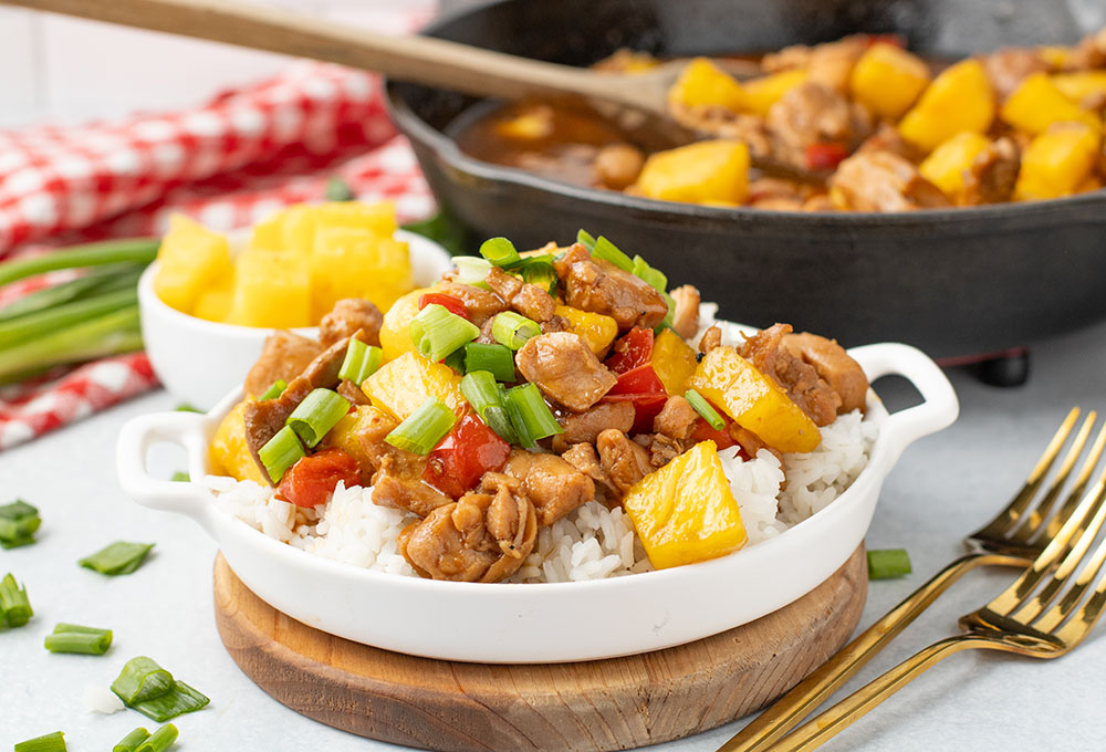 picture of freshly made pineapple chicken in a white bowl with a cast iron pan in the background